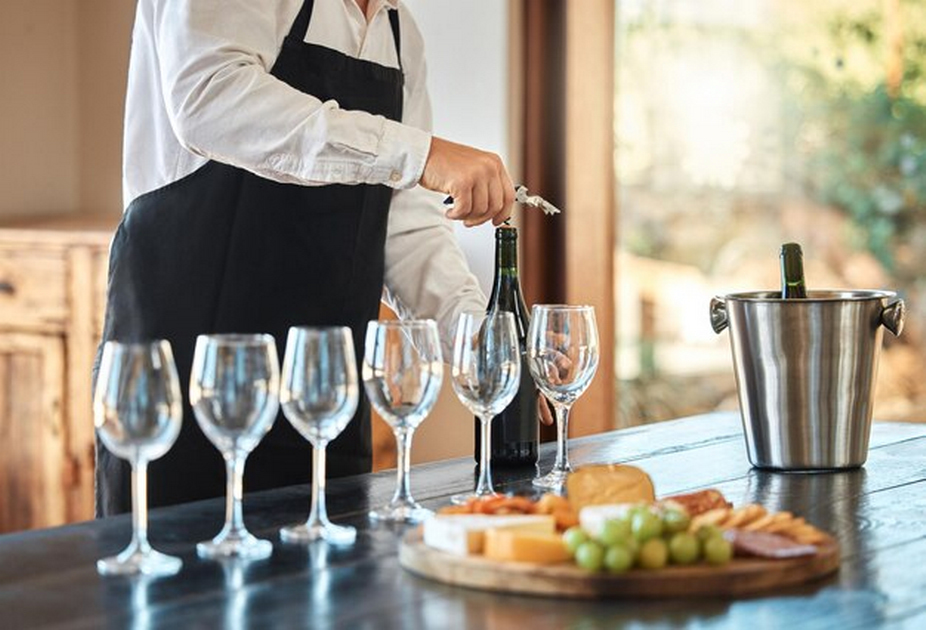 Pouring wine into wine glasses, wine, cheese, fruits, and crackers on a wooden platter